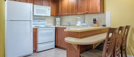 Una cocina con armarios de madera, un refrigerador blanco, un microondas, una cafetera y un lavabo.