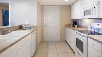 Una cocina moderna con armarios blancos, un lavamanos doble, un tostador, una cafetera y un microondas.