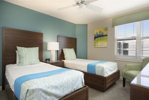 A hotel room with two beds, a ceiling fan, a window with blinds, and a painting on the wall.
