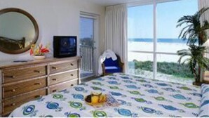 A bedroom with a bed, a ceiling fan, a dresser, a television, and a large window with a view of the ocean. - GullWing Beach Resort (Fort Myers Beach)