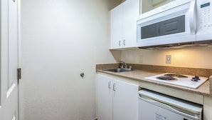 A compact kitchen with white cabinets, a built-in microwave, a granite countertop, and a stainless steel sink. - HomeTowne Studios by Red Roof Atlanta - Chamblee (Chamblee)