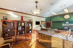 A reception area with a wooden reception desk, a clock, and a wall sign for 'HOMETOWN STUDIOS'. - HomeTowne Studios by Red Roof Atlanta - Chamblee (Chamblee)