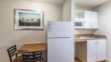 Een functionele keuken met een koelkast, magnetron en een eethoek met tafel en stoelen.