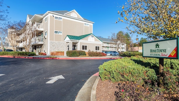 A multi-story building with a green roof, a signboard for 'HomeTowe Studios by RedRoof', and a parking lot with directional arrows. - HomeTowne Studios by Red Roof Atlanta - Chamblee (Chamblee)