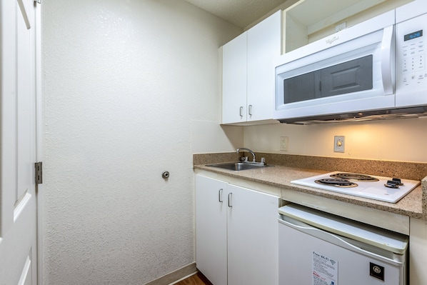Una cocina compacta con armarios blancos, microondas, estufa y lavavajillas.