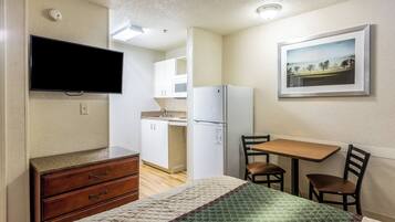 Una habitación pequeña con cama, escritorio, silla, televisión, refrigerador y microondas.