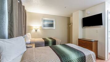 A hotel room with two beds, a TV, a bedside table, a lamp, and a framed picture on the wall.