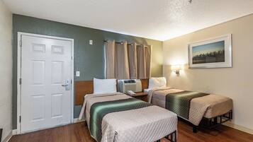 A hotel room with two beds, a door, a nightstand, a lamp, and a picture on the wall.