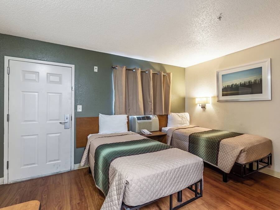 A hotel room with two beds, a door, a nightstand, a lamp, and a picture on the wall.