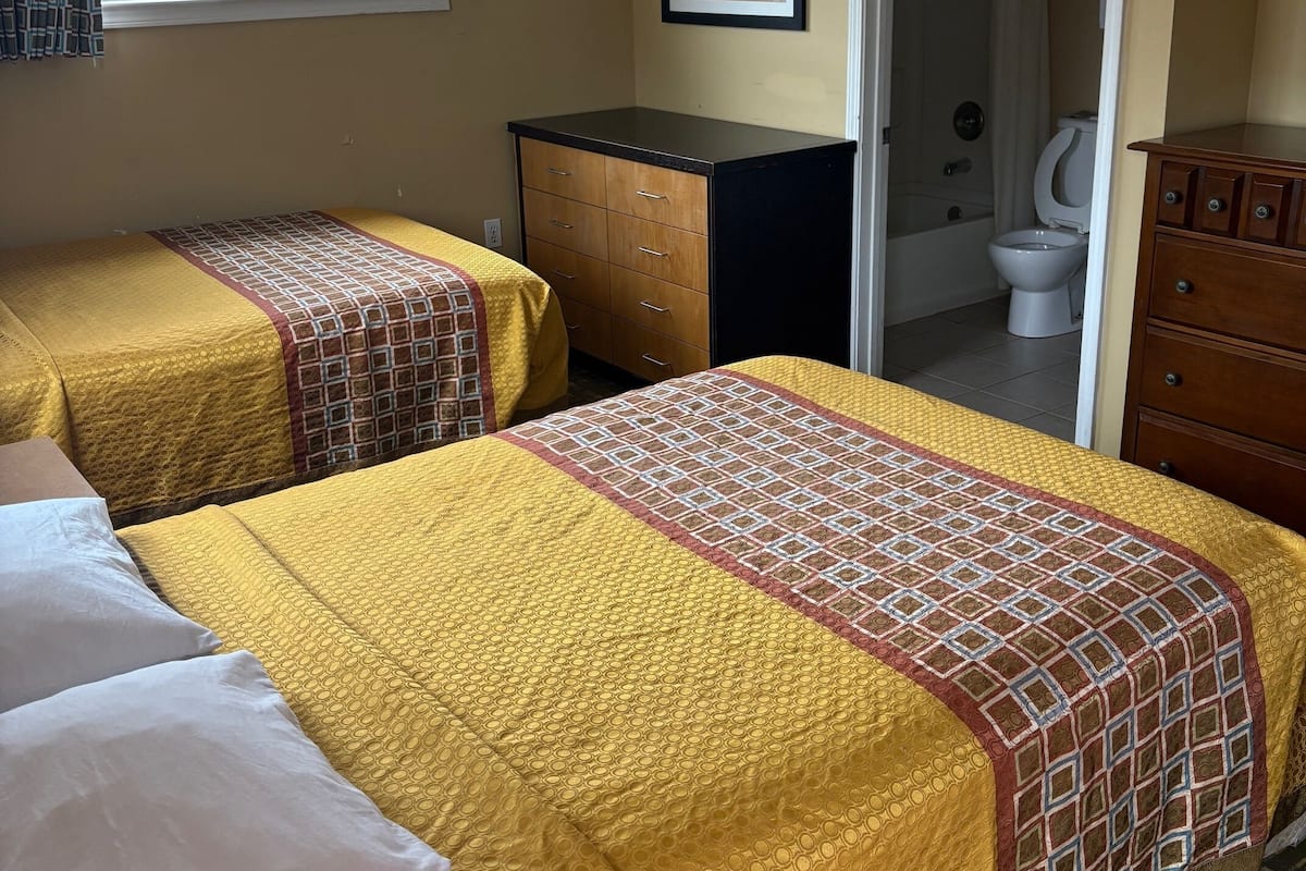 A hotel room with two beds, a dresser, a framed picture on the wall, and a bathroom visible through an open door.
