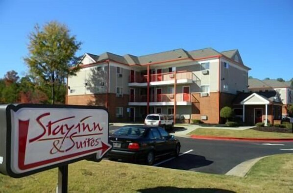 Edificio de StayInn & Suites de dos pisos, con una decoración en rojo y blanco, y un estacionamiento con un coche negro.