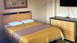 A hotel room with a bed, a dresser, a TV, and a wall with framed pictures. - Stay Inn & Suites (Stockbridge)