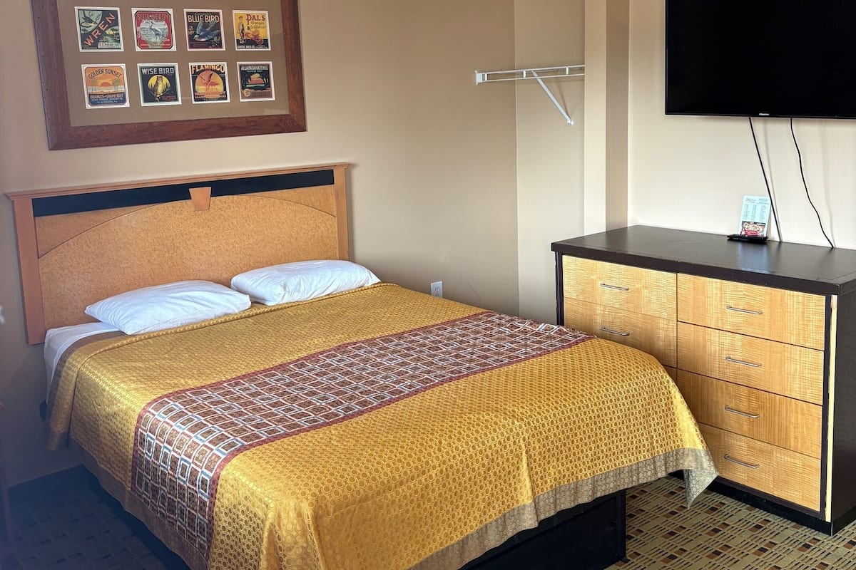 A hotel room with a bed, a dresser, a TV, and a wall with framed pictures.