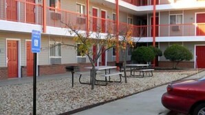 A multi-story building with a red and white color scheme, outdoor seating, and a parking area. - Stay Inn & Suites (Stockbridge)