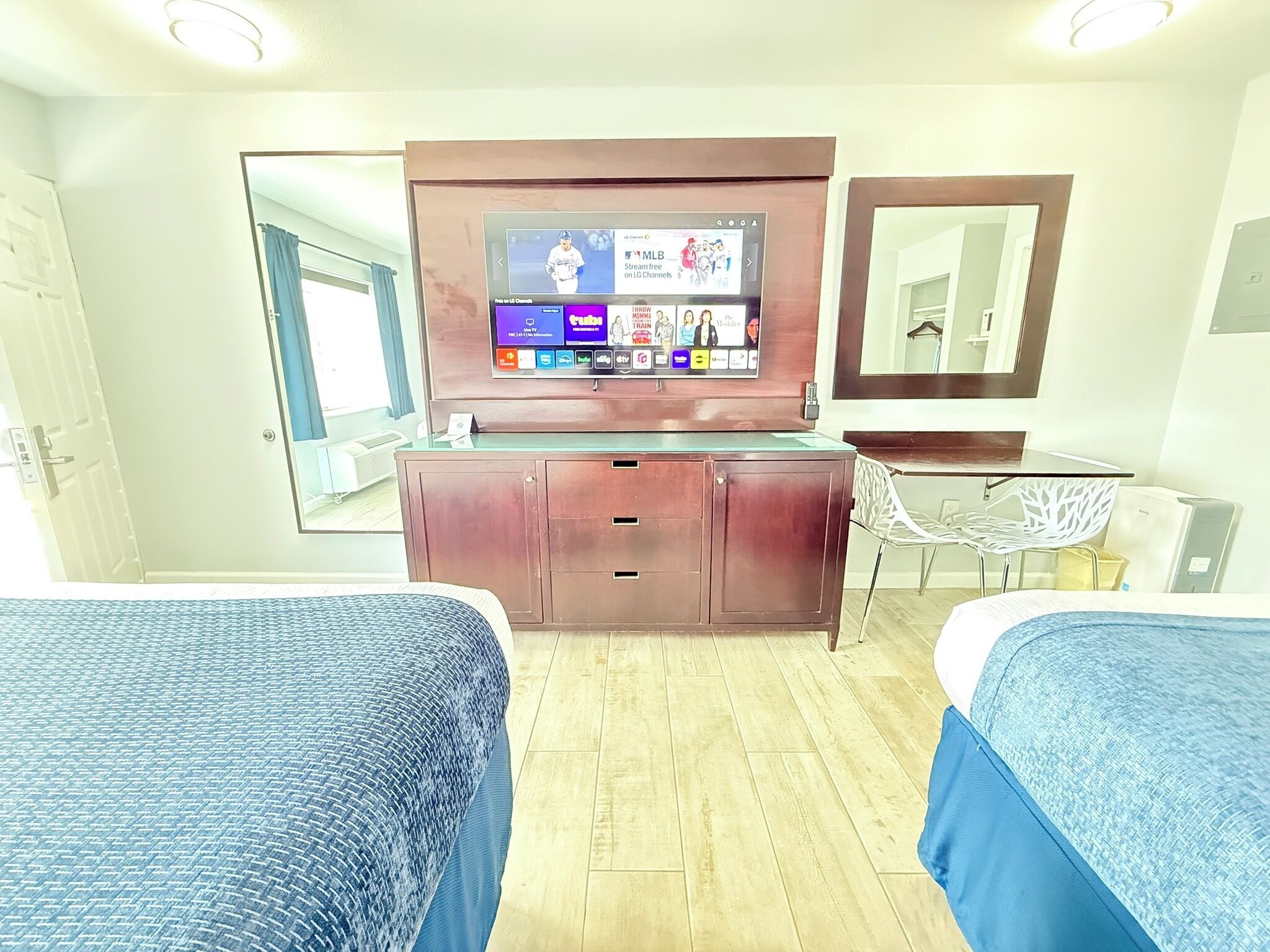 A hotel room with two beds, a TV mounted on the wall, a mirror, a desk, and a chair.