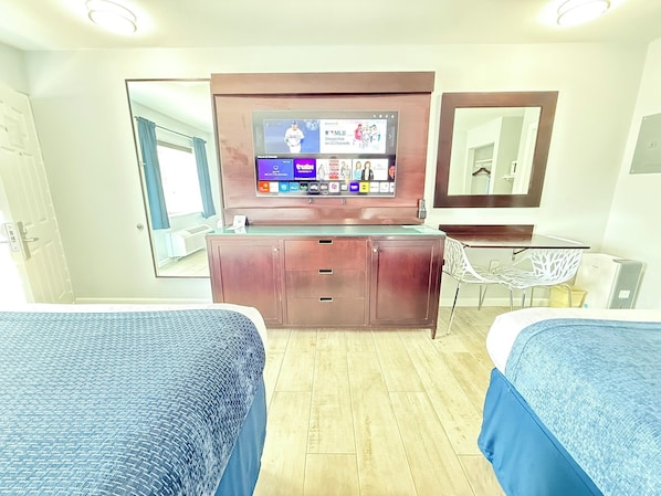 A hotel room with two beds, a TV mounted on the wall, a mirror, a desk, and a chair.