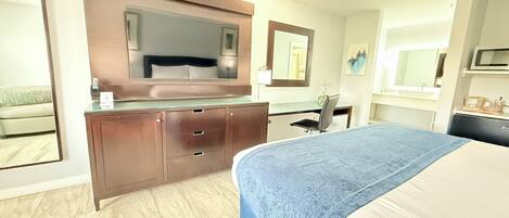 A hotel room with a bed, a desk with a chair, a large mirror, and a television.
