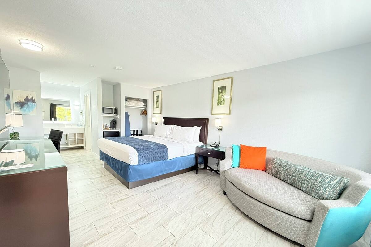 A hotel room with a bed, a desk, a sofa, and a bathroom visible in the background.