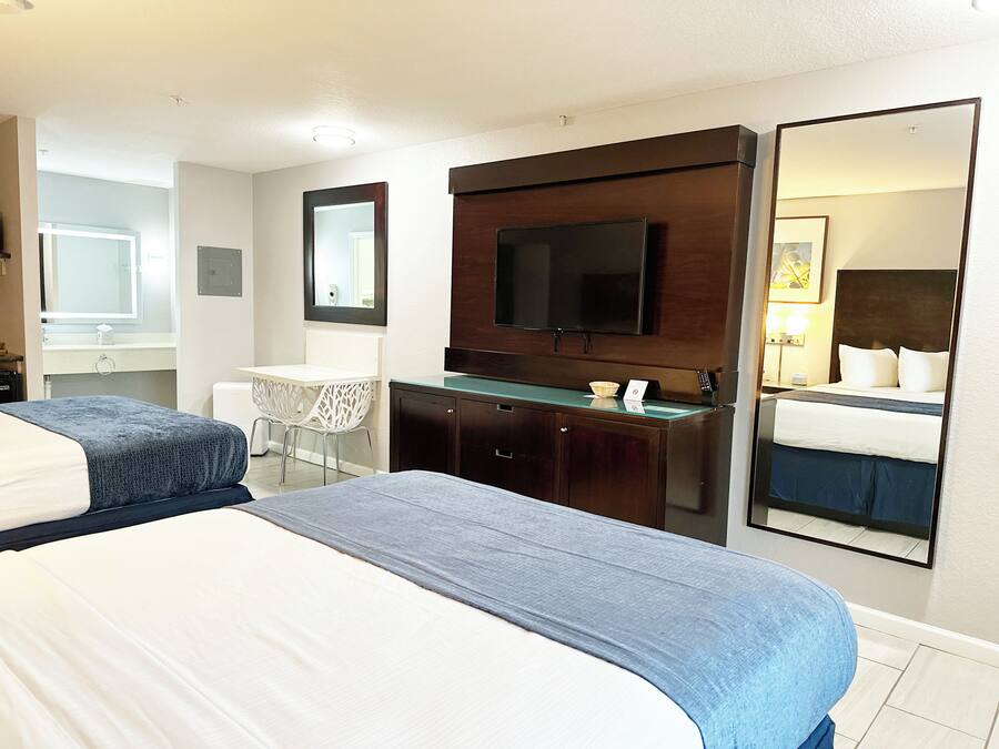 Habitación de hotel con dos camas, un escritorio, un espejo, un televisor y un baño.