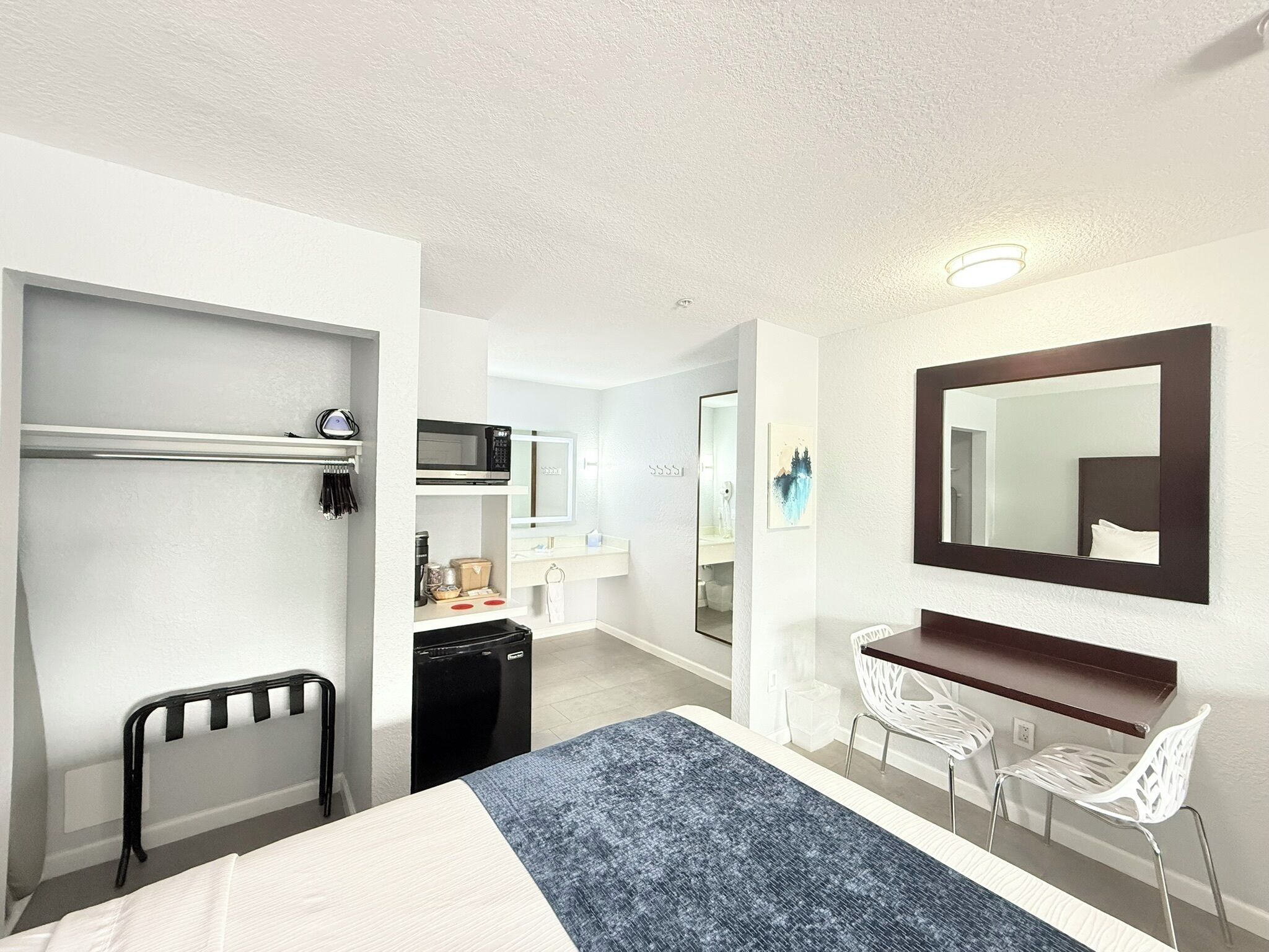 Une chambre d’hôtel équipée d’un lit, d’un bureau, d’une chaise, d’un four à micro-ondes, d’un réfrigérateur et d’un grand miroir.