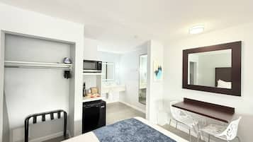 Une chambre d’hôtel équipée d’un lit, d’un bureau, d’une chaise, d’un four à micro-ondes, d’un réfrigérateur et d’un grand miroir.