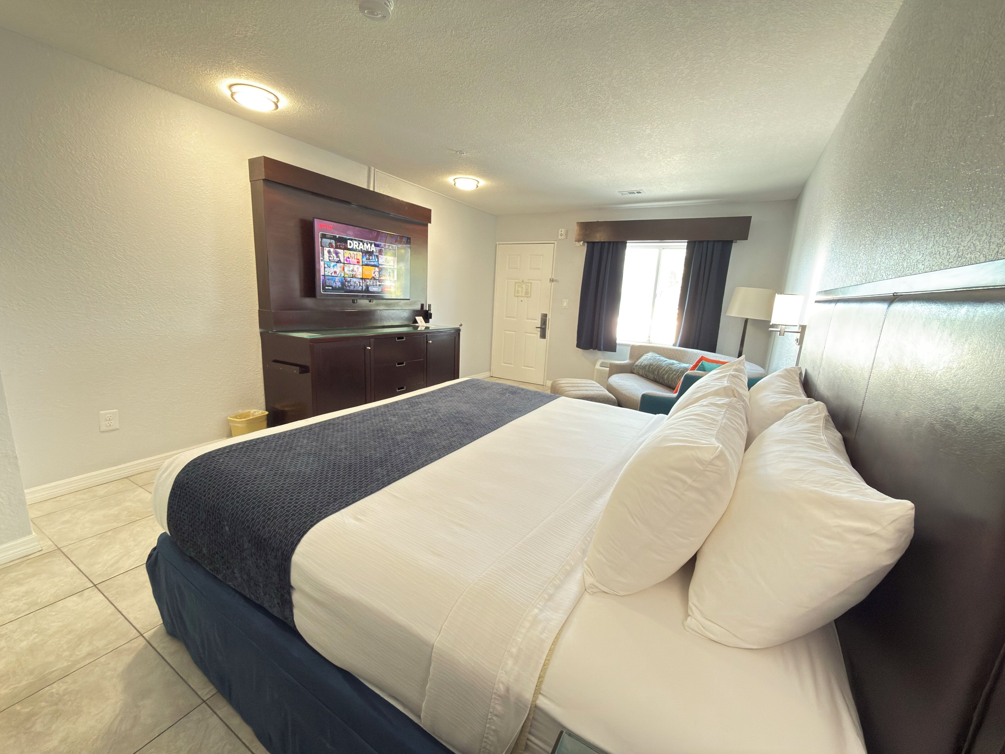 Une chambre d’hôtel avec un grand lit, un téléviseur fixé au mur, un bureau avec un ordinateur et une fenêtre avec des rideaux.