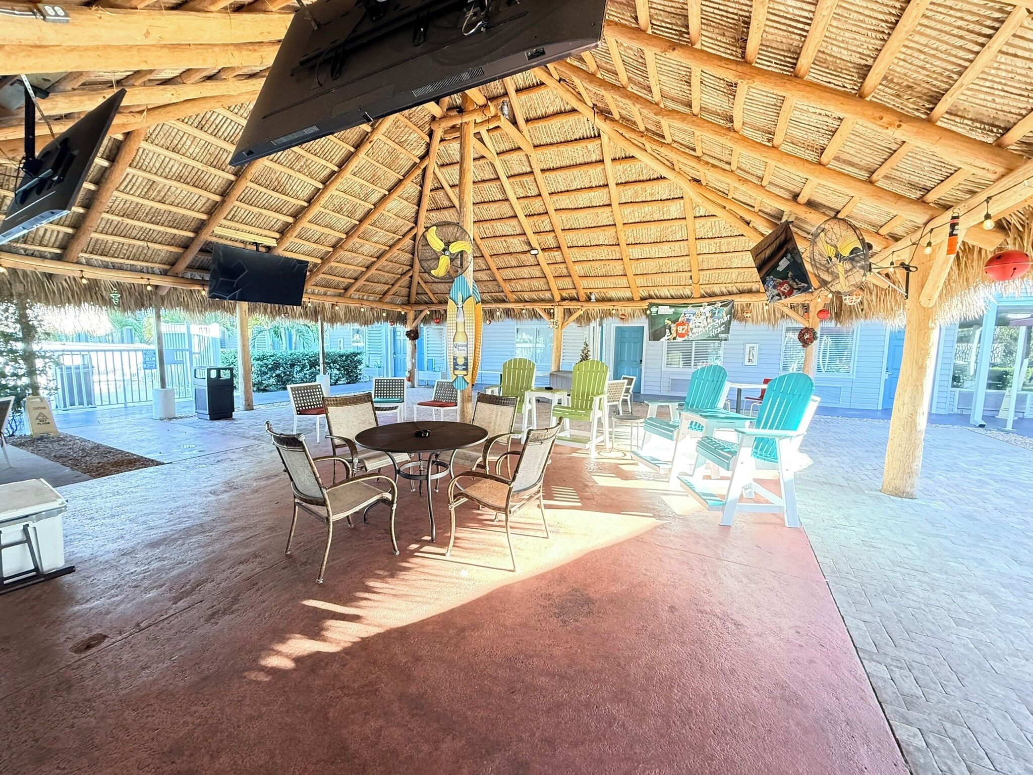 A covered outdoor seating area with a thatched roof, tables, and chairs.