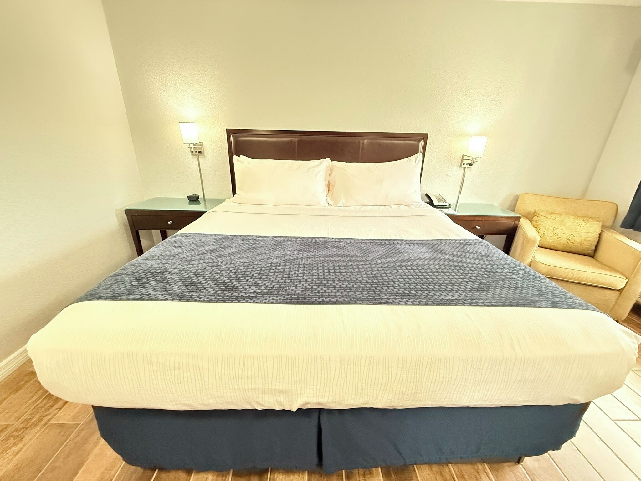 A hotel room with a large bed, a bedside table with a lamp, a chair, and a nightstand with a phone.