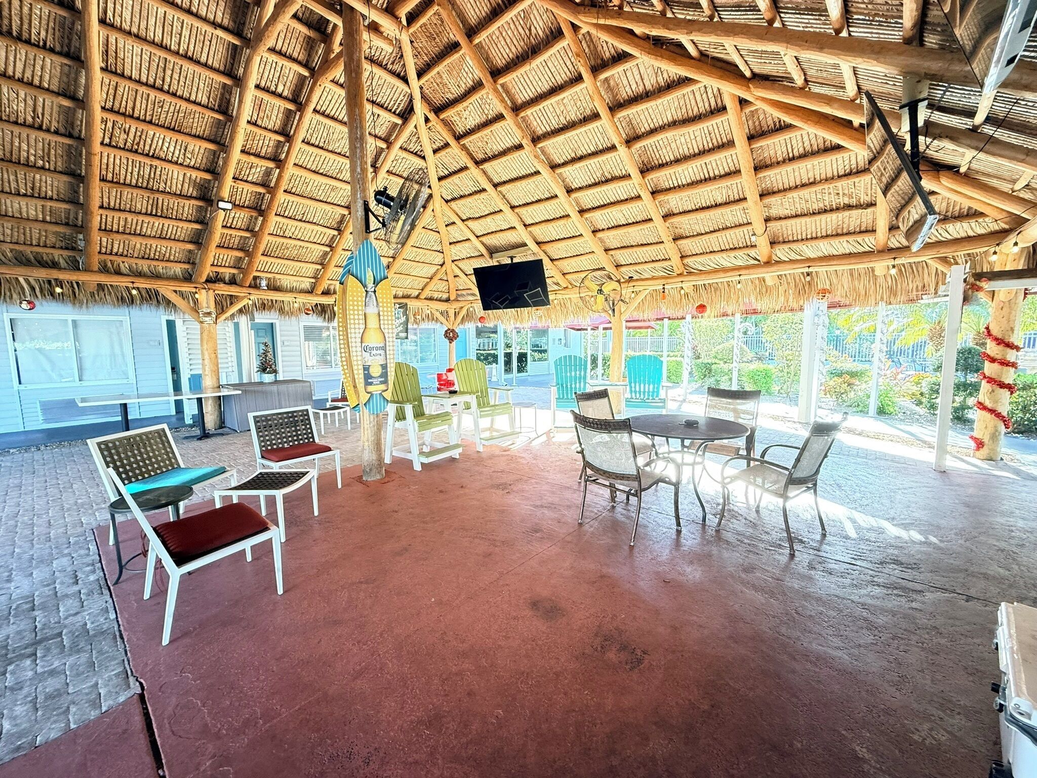 A covered outdoor seating area with chairs and tables, a thatched roof, and a TV screen.. Lantern Inn & Suites