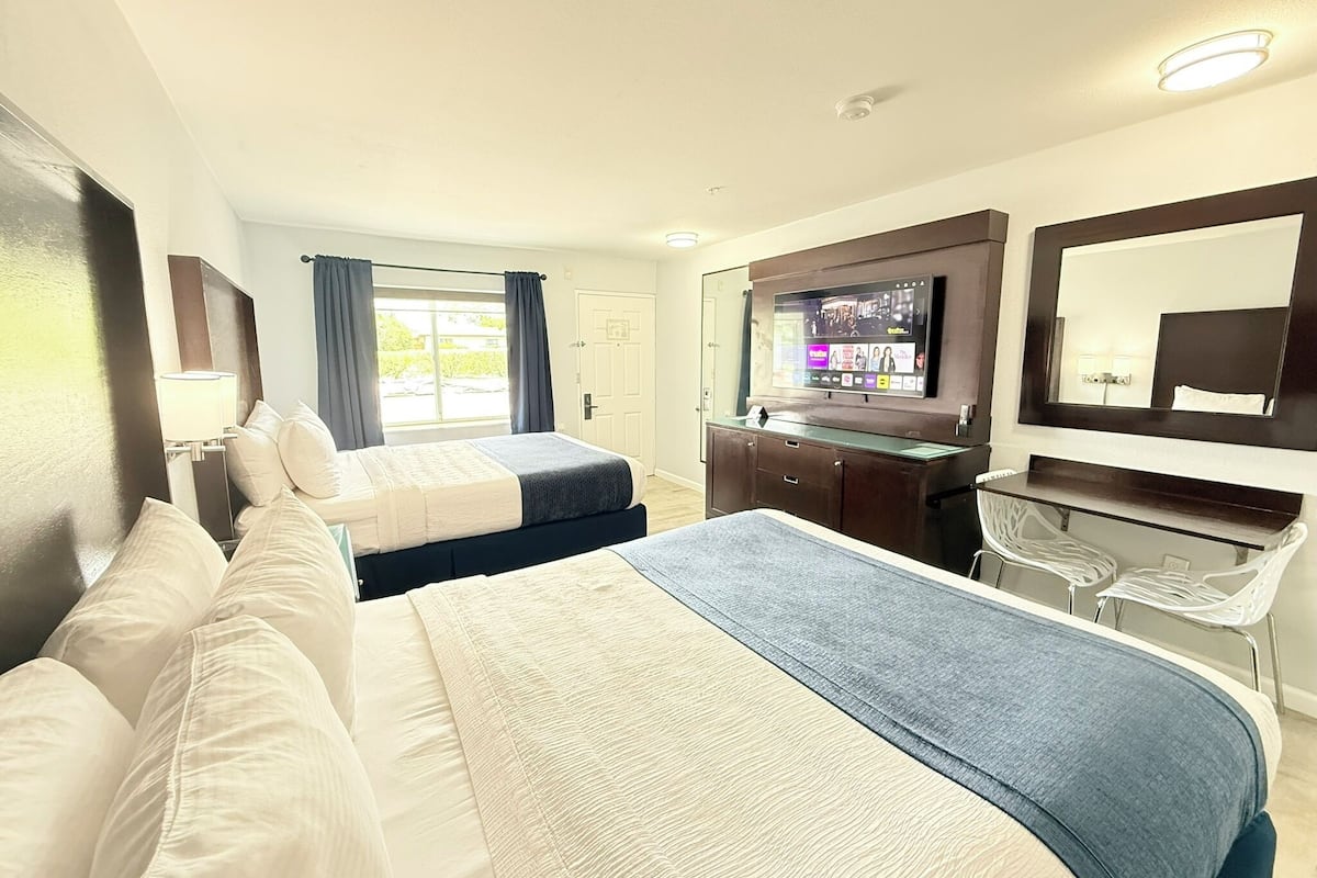 A hotel room with two beds, a desk, a TV, and a mirror.