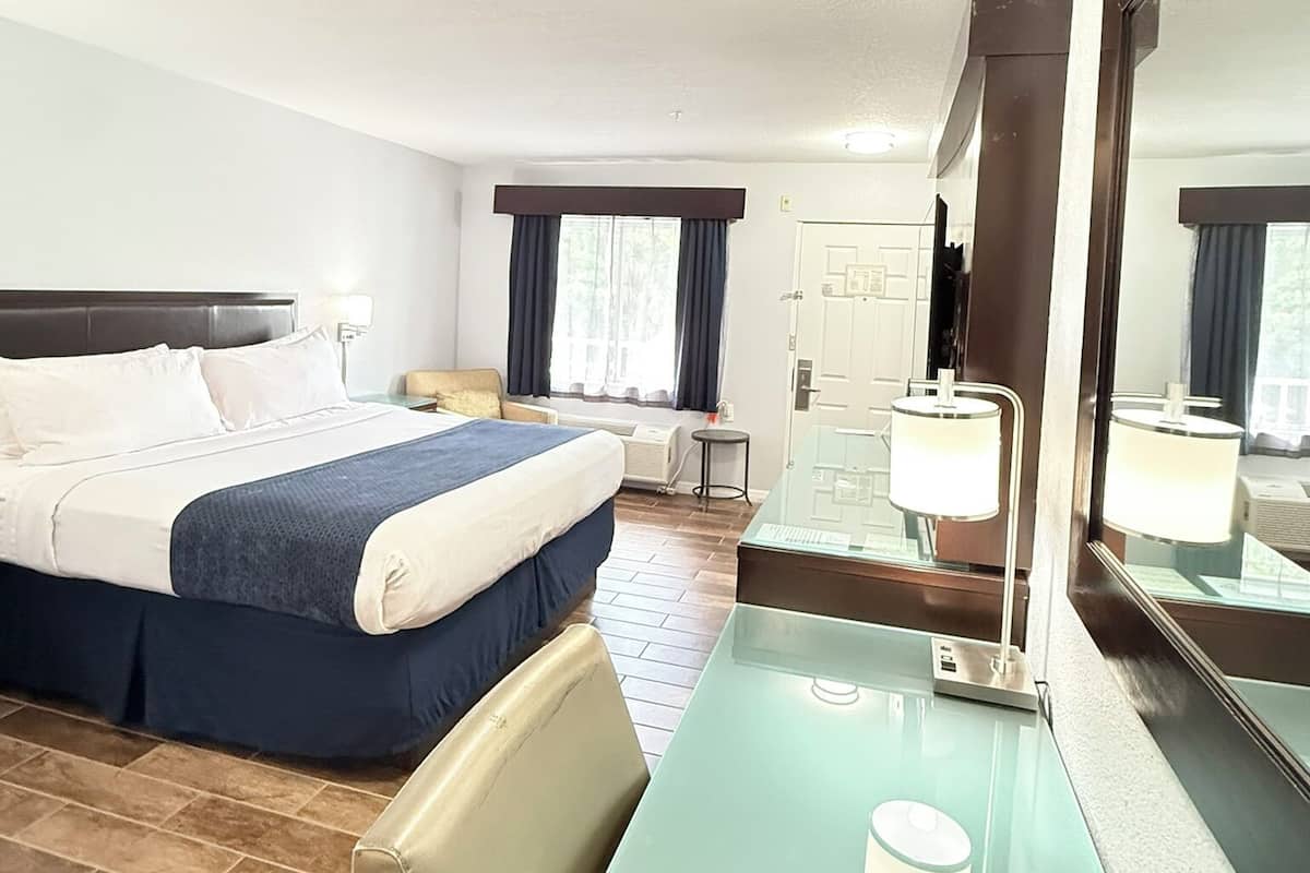 A hotel room with a bed, a desk, a chair, a mirror, and a window with curtains.