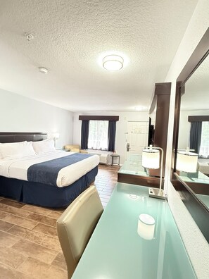 Ett hotellrum med en säng, ett skrivbord, en stol, en spegel och ett fönster med gardiner.