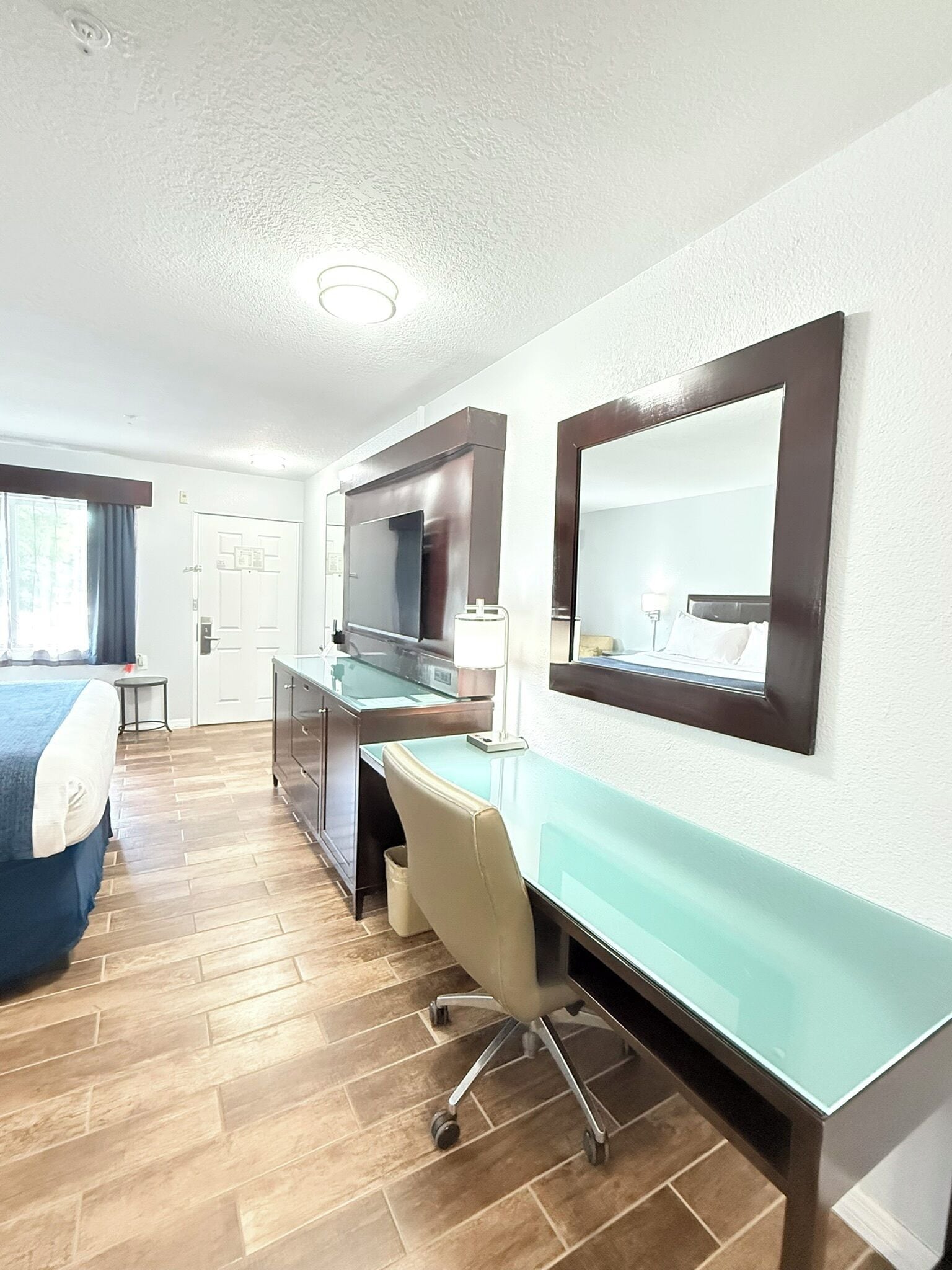 Ett hotellrum med en säng, ett skrivbord, en stol och en stor spegel.