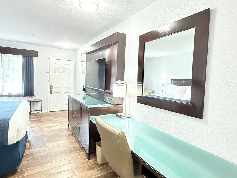Ett hotellrum med en säng, ett skrivbord, en stol och en stor spegel.