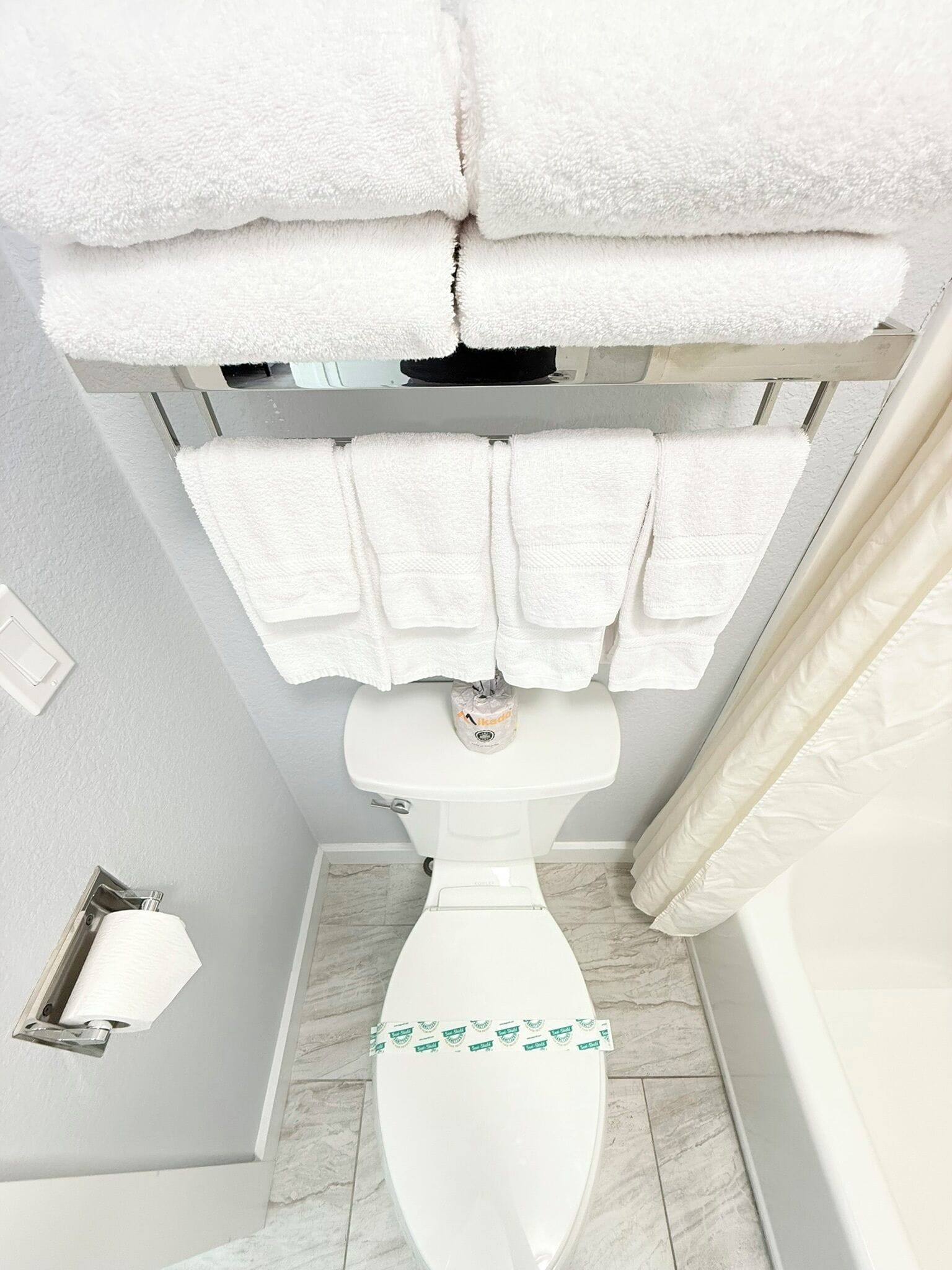 Une salle de bain avec des toilettes, un rouleau de papier toilette et une pile de serviettes blanches.