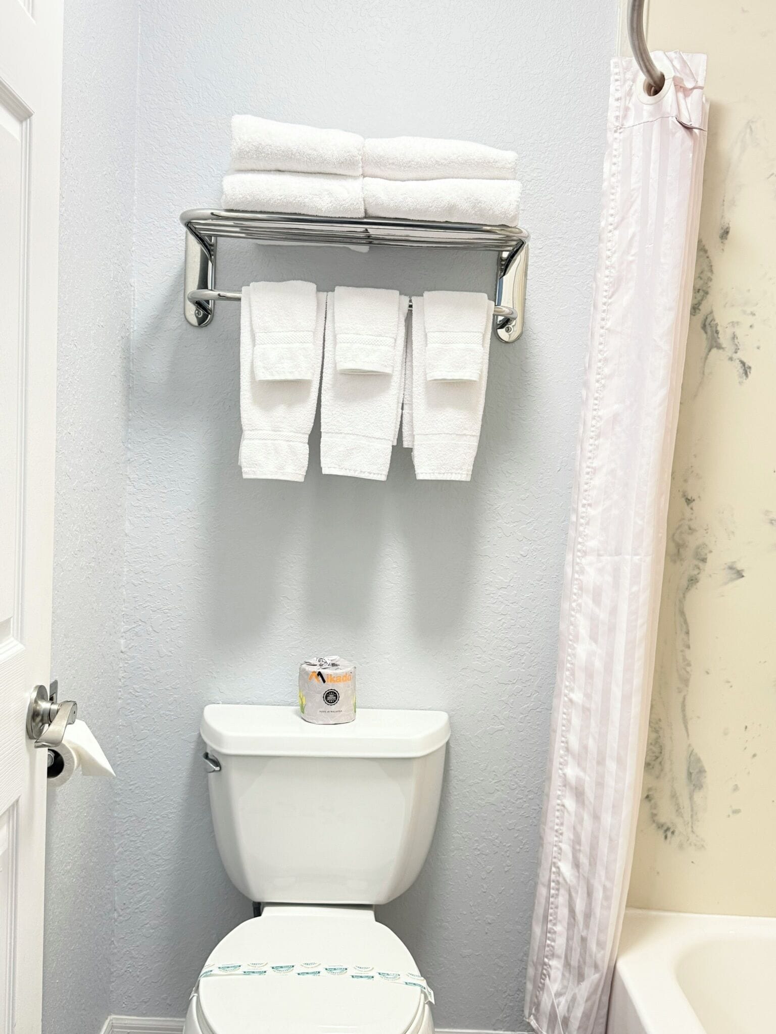 A bathroom with a toilet, a towel rack with folded towels, and a toilet paper dispenser.
