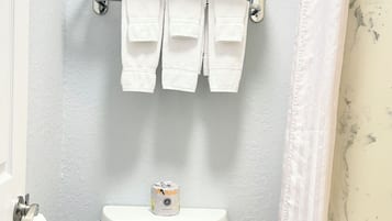 A bathroom with a toilet, a towel rack with folded towels, and a toilet paper dispenser.
