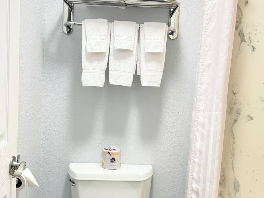 A bathroom with a toilet, a towel rack with folded towels, and a toilet paper dispenser.