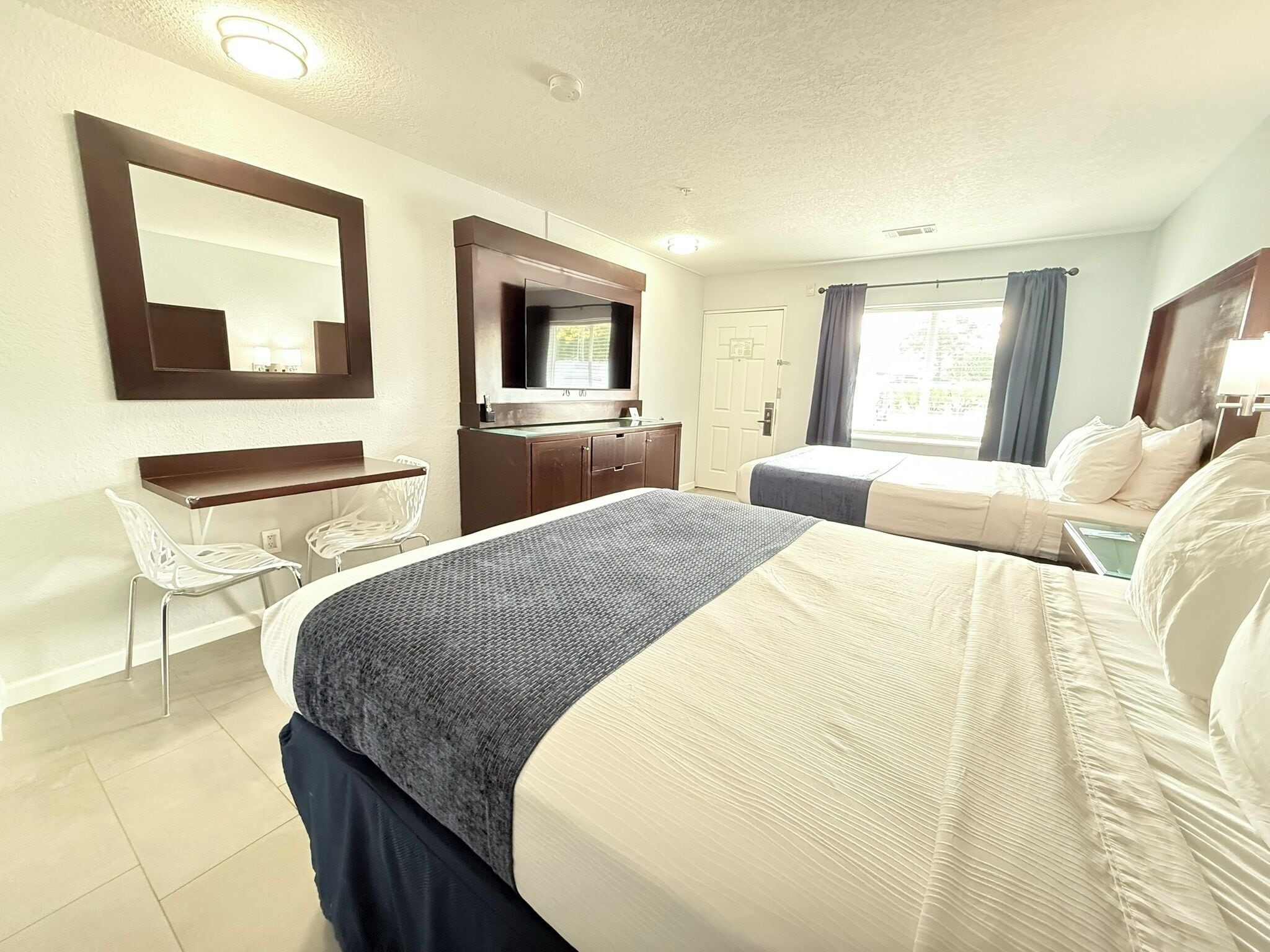 Habitación de hotel con cama, escritorio, silla, televisor y ventana con cortinas.
