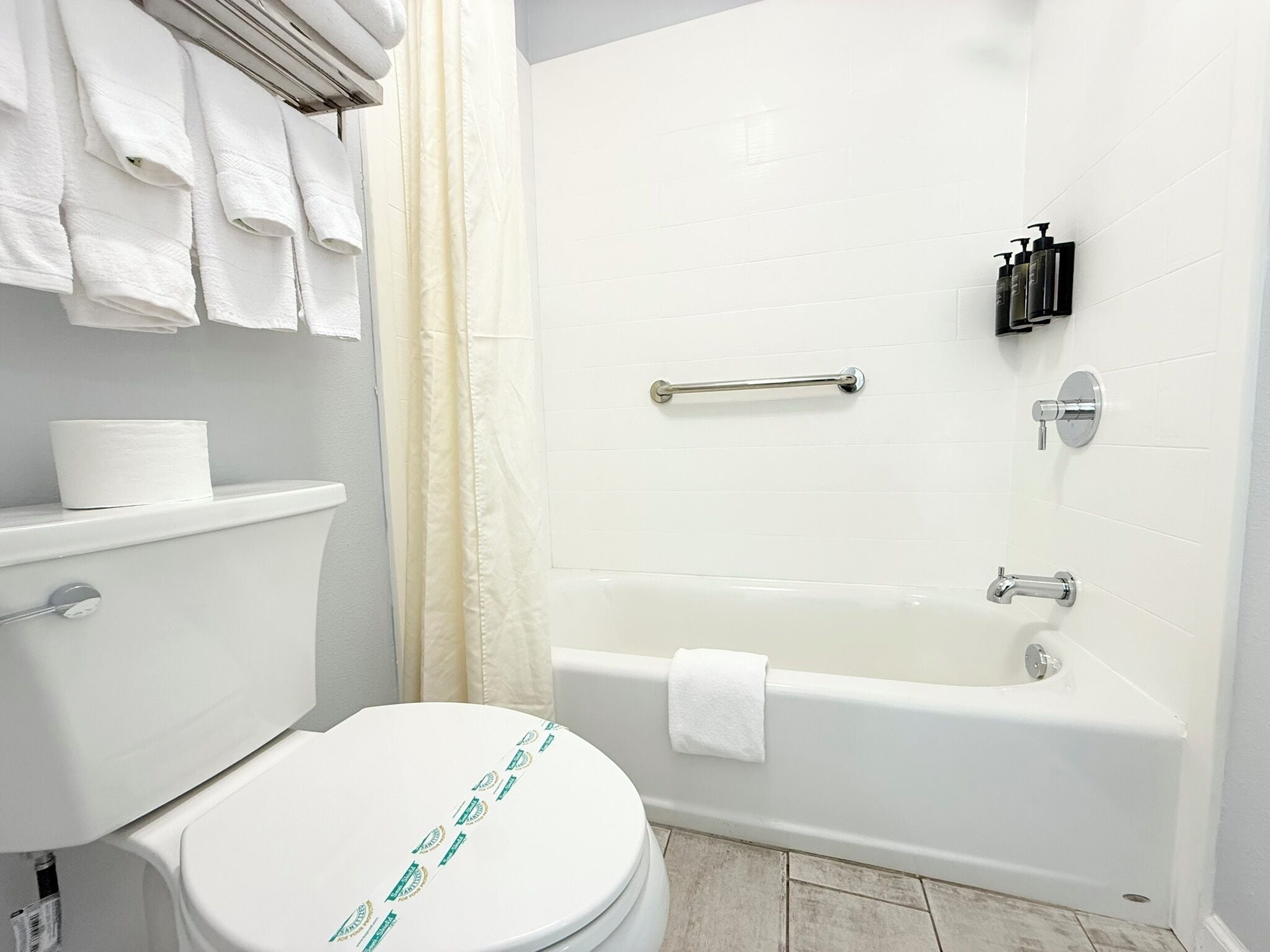 A bathroom with a toilet, a bathtub, a shower curtain, and toiletries on the wall.