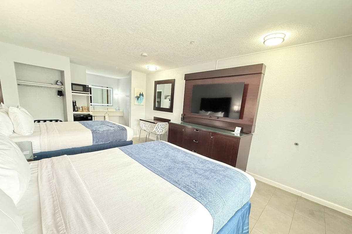 A hotel room with two beds, a TV, a desk, and a chair.