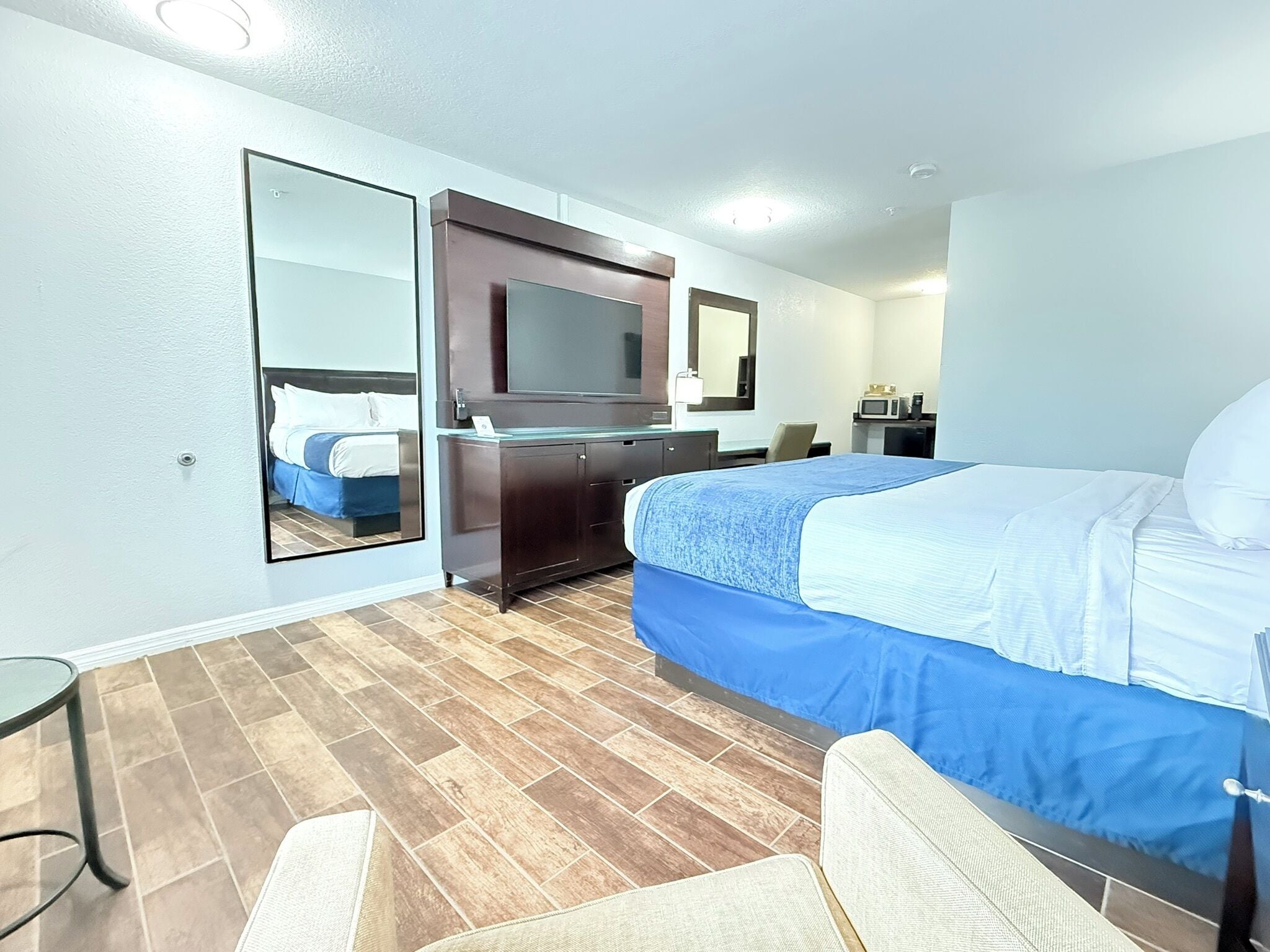 Habitación de hotel con cama, cómoda, espejo, televisor, microondas y una silla.