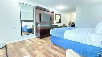 A hotel room with a bed, a dresser, a mirror, a television, a microwave, and a chair.