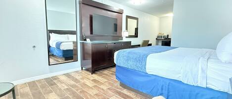 Habitación de hotel con cama, cómoda, espejo, televisor, microondas y una silla.