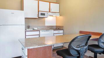 A compact kitchen with a refrigerator, microwave, and dishwasher, a granite countertop, and two black office chairs.