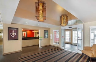 Un vestíbulo de hotel con una recepción, un área de espera con un sofá y una entrada con puerta de vidrio.