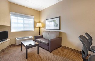 Habitación de hotel con sofá, una mesita, televisor, lámpara y un cuadro en la pared.