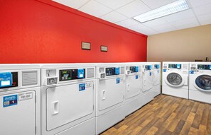 A laundry facility with multiple washing machines and dryers, a red wall, and a wooden floor. - Extended Stay America Suites Secaucus New York City Area (Secaucus)