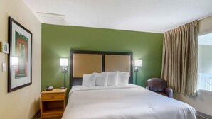 A hotel room with a large bed, a nightstand, a chair, and a window with curtains. - Extended Stay America Suites Secaucus New York City Area (Secaucus)