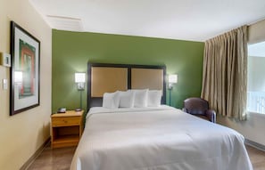 Habitación de hotel con una cama grande, una mesita de noche, una silla y una ventana con cortinas.